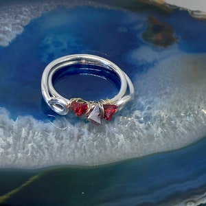May include: A silver ring with three red gemstone accents. The ring is on a blue and white agate background.