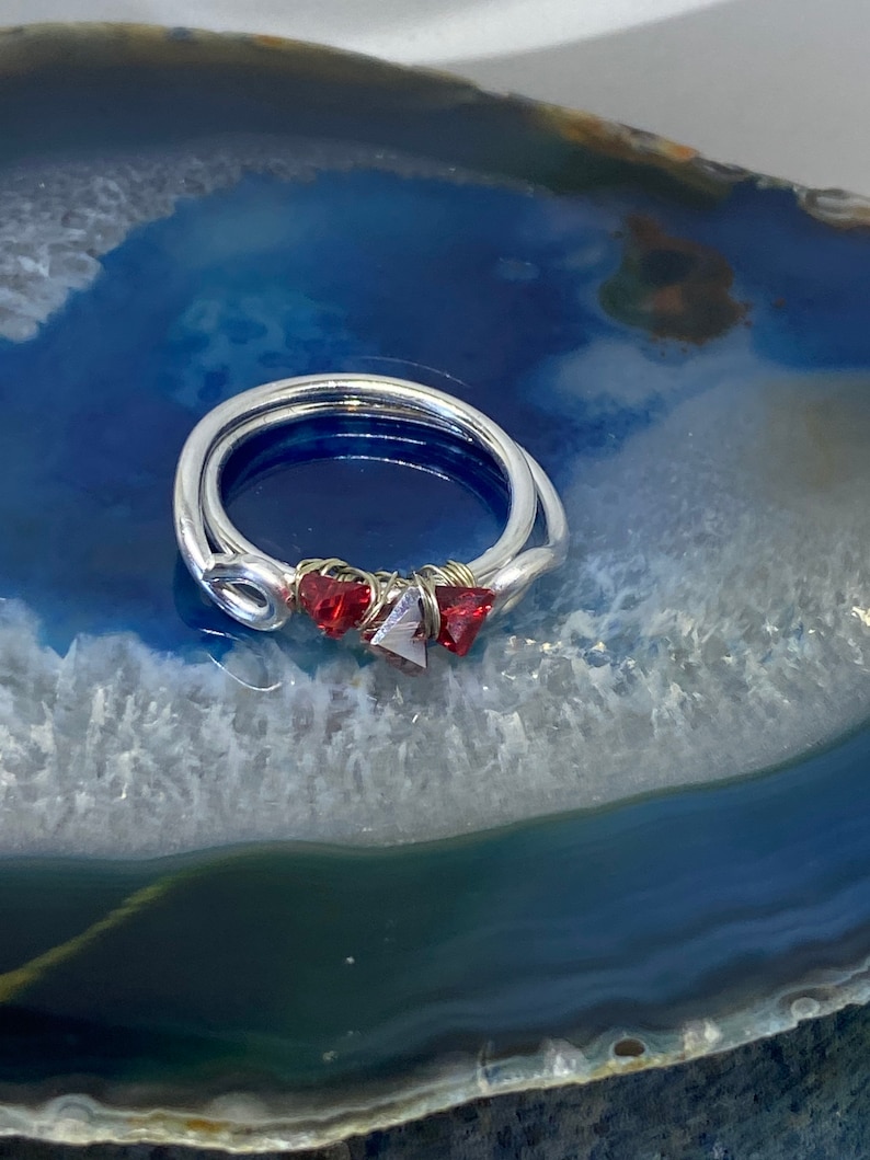 May include: A silver ring with three red gemstone accents. The ring is on a blue and white agate background.