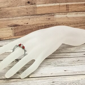 May include: A silver ring with three red stones set in a claw setting.