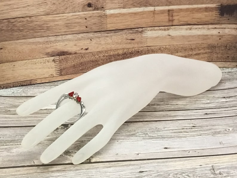 May include: A silver ring with three red stones set in a claw setting.