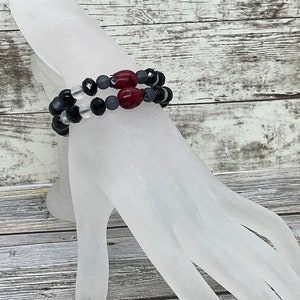 May include: A double-strand bracelet with black, white, and gray beads, accented with two red beads.