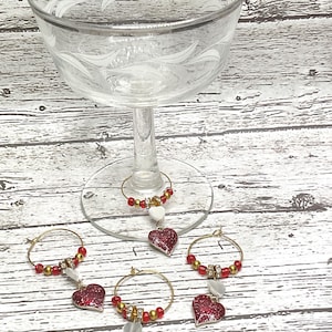 Puede incluir: Conjunto de cinco charms para copa de vino con forma de corazón rojo con purpurina, anillos dorados y cuentas blancas.