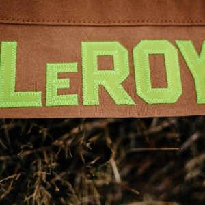 May include: A brown canvas bag with the name "LEROY" stitched in green thread.