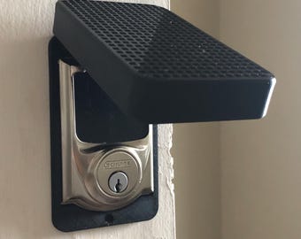 May include: A black plastic door lock cover with a Schlage lock underneath. The cover has a textured surface and is hinged to open.