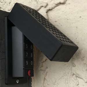May include: A black keypad with a black cover that is partially open. The keypad has numbers 5, 6, 7, 8, 9, and 0 on it. The cover has a grid pattern.