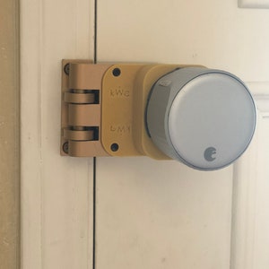 May include: A gold-coloured smart door lock with a round, grey keypad. The lock is mounted on a white door.