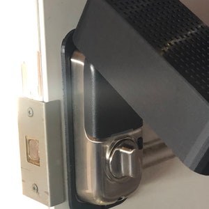 Può includere: Una serratura per porte argentata con una copertura nera. La copertura ha una superficie testurizzata ed è fissata al telaio della porta.