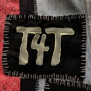 May include: A black fabric patch with white stitching around the edges. The patch has the text "T4T" written in white paint.