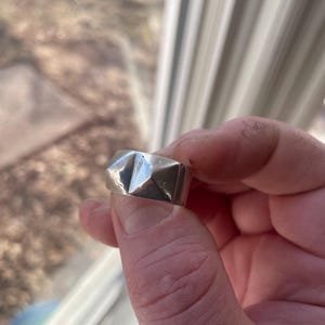 May include: A silver ring with a geometric design. The ring is made of metal and has a textured surface.