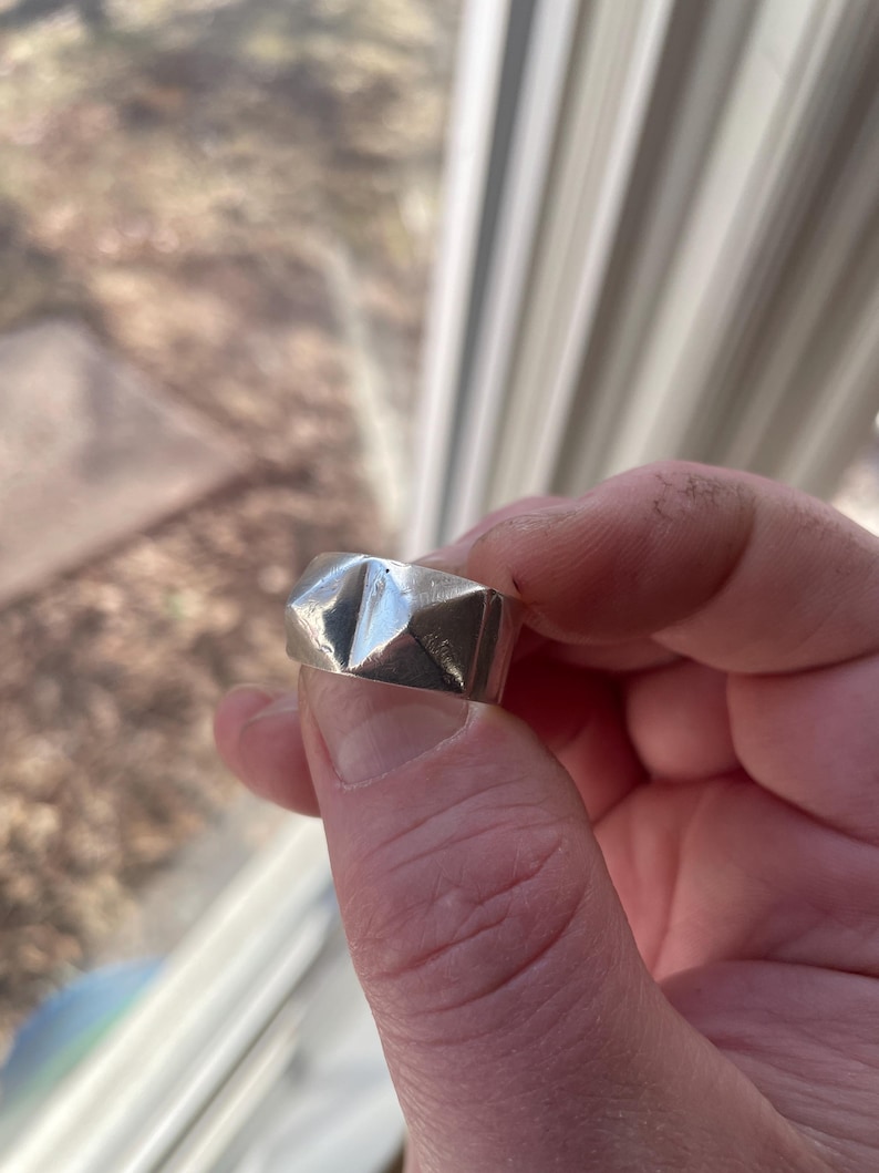May include: A silver ring with a geometric design. The ring is made of metal and has a textured surface.
