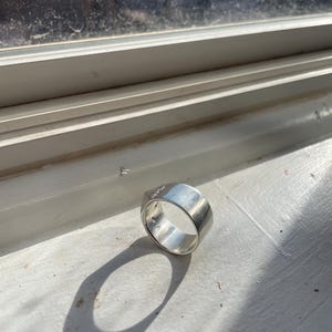 May include: A silver ring with a wide band and a smooth, polished finish.