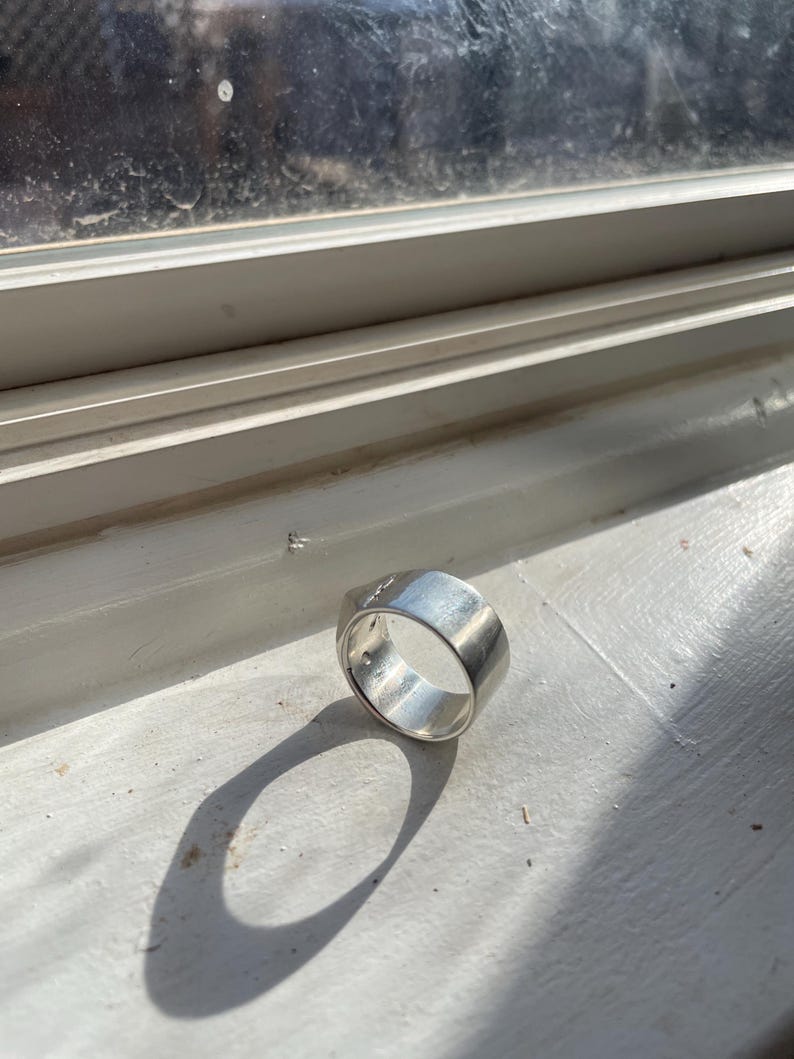 May include: A silver ring with a wide band and a smooth, polished finish.