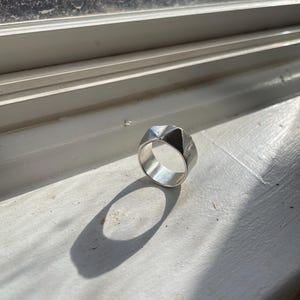 May include: A silver ring with a geometric design. The ring is made of a smooth metal and has a shiny finish.