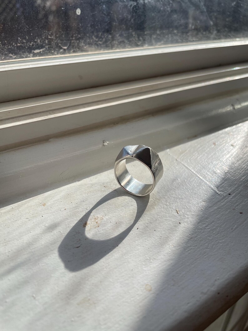 May include: A silver ring with a geometric design. The ring is made of a smooth metal and has a shiny finish.