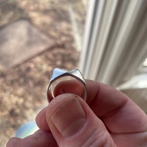 May include: A silver ring with a unique, angular design. The ring is made of metal and has a smooth, polished finish.