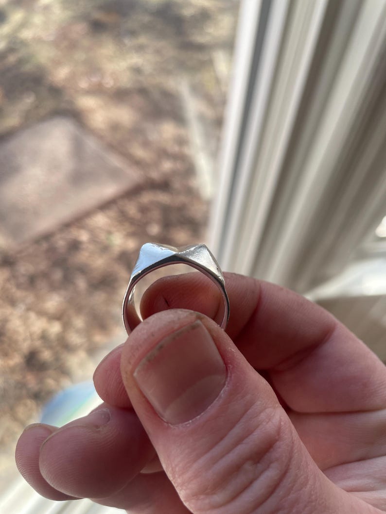 May include: A silver ring with a unique, angular design. The ring is made of metal and has a smooth, polished finish.