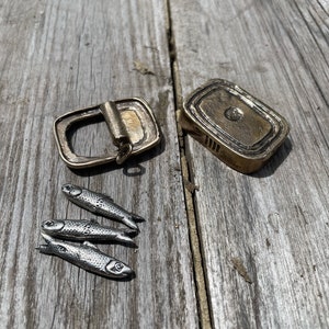 May include: A set of four silver-coloured fish charms, a gold-coloured buckle, and a gold-coloured rectangular plate with a raised design.