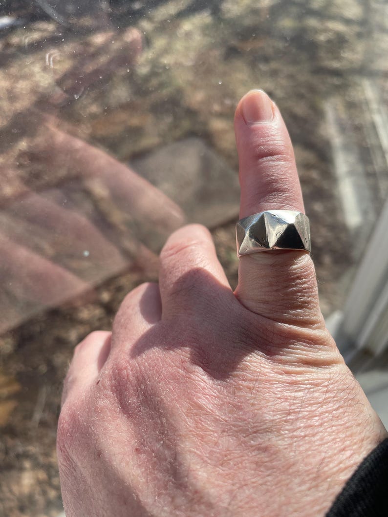 May include: A silver ring with a geometric design. The ring is worn on a finger.