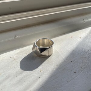 May include: A silver ring with a geometric design. The ring is made of metal and has a textured surface.