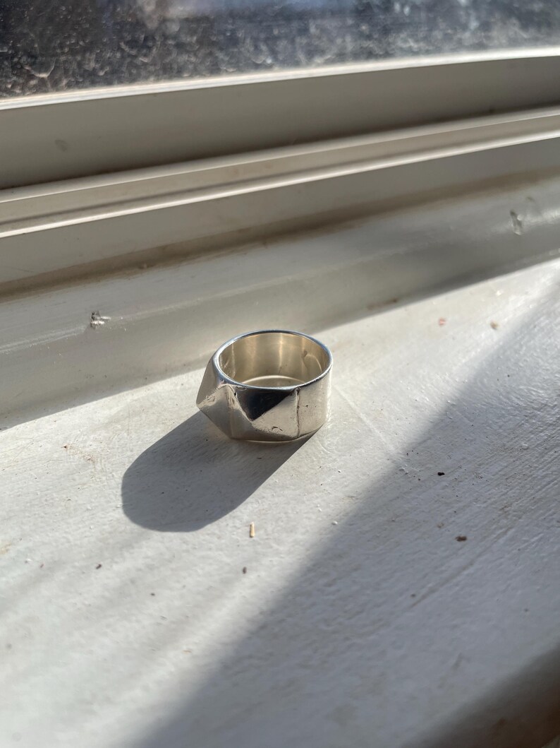 May include: A silver ring with a geometric design. The ring is made of metal and has a textured surface.