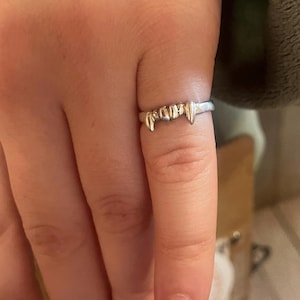 May include: A silver ring with a design of fangs. The ring is worn on a person's finger.