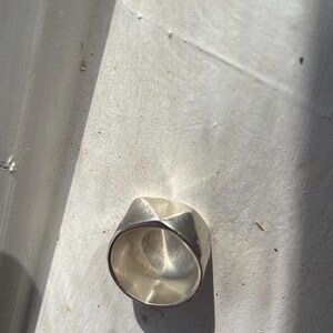 May include: A silver ring with a geometric design. The ring is made of a smooth, polished metal and has a unique, modern look.