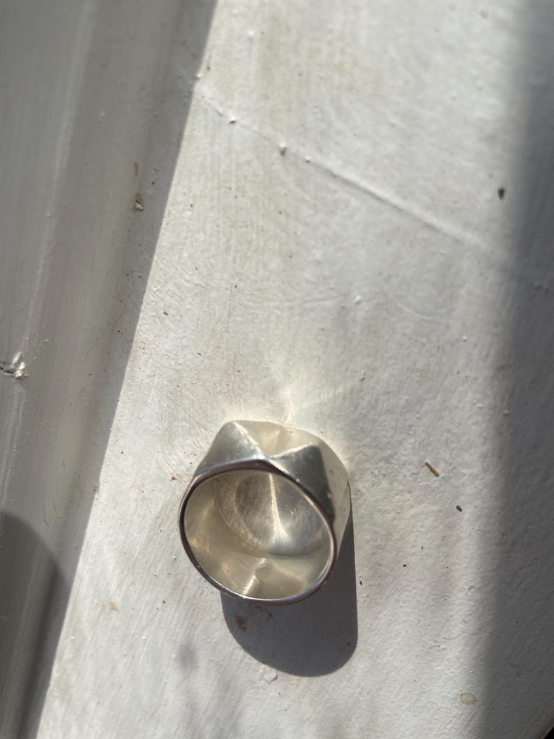 May include: A silver ring with a geometric design. The ring is made of a smooth, polished metal and has a unique, modern look.