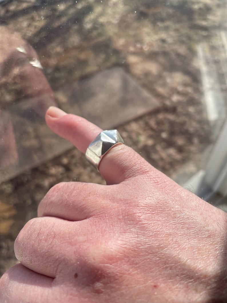 May include: A silver ring with a geometric design. The ring is worn on a finger.