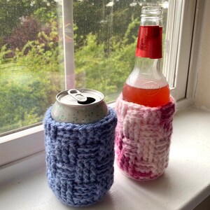 May include: Two crocheted beverage insulators, one in pink and white and one in blue. The pink and white insulator is on a glass bottle, and the blue insulator is on a silver can.