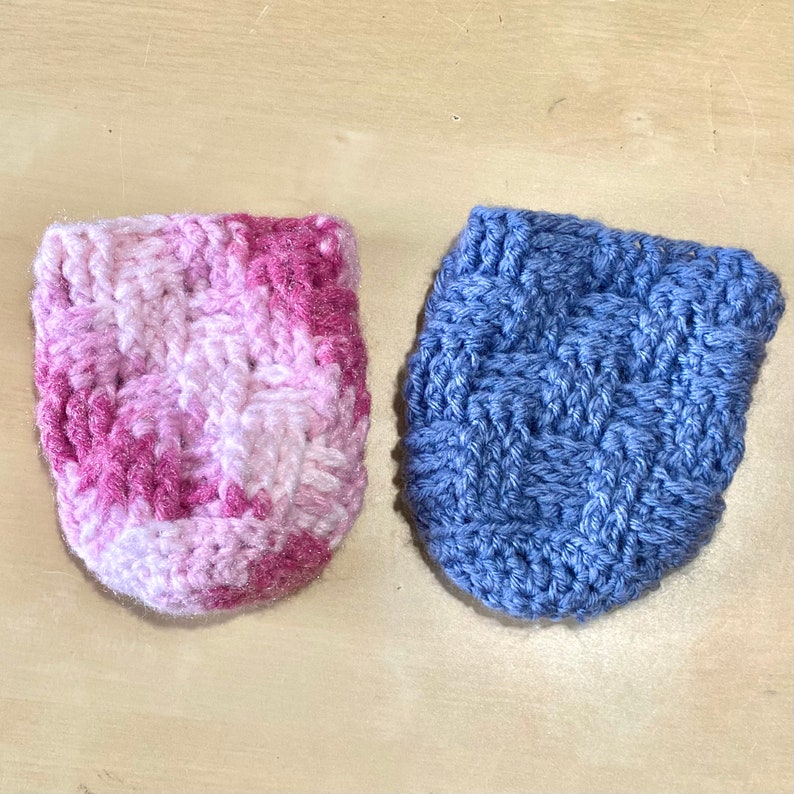 May include: Two crocheted pouches, one in pink and white ombre and one in blue. Both pouches are made with a simple stitch pattern.