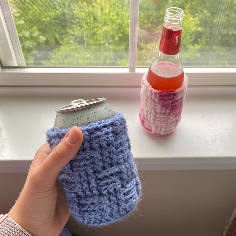 May include: Two crocheted beverage insulators, one in pink and white and one in blue. The pink and white insulator is on a glass bottle, while the blue insulator is on a can.