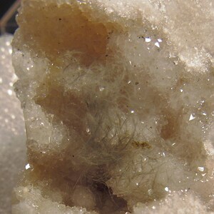 May include: A white geode with a cavity filled with clear quartz crystals and a cluster of green fibrous crystals.
