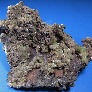May include: A rough, gray and green rock with a textured surface. The rock has a variety of mineral formations, including small, green crystals.