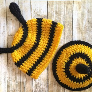 May include: A handmade crochet bee costume set, featuring a yellow and black striped hat with antennae and a matching round bottom piece. The set is designed with a textured, ribbed pattern.