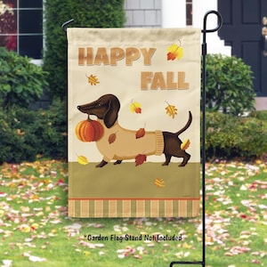 May include: A decorative garden flag featuring a dachshund dog carrying a pumpkin, wearing a sweater, and surrounded by autumn leaves. The flag reads "HAPPY FALL" in brown letters against a beige background. The flag is displayed on a black metal stand.