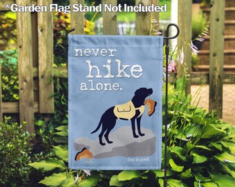 May include: A blue garden flag with a black Labrador Retriever on a rock with a hiking boot in its mouth. The flag reads "never hike alone." and "dog is good."