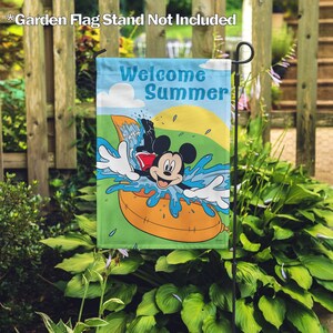 May include: A garden flag featuring Mickey Mouse in a yellow inner tube, splashing in blue water. The flag has a green background with the text "Welcome Summer" in blue and white.