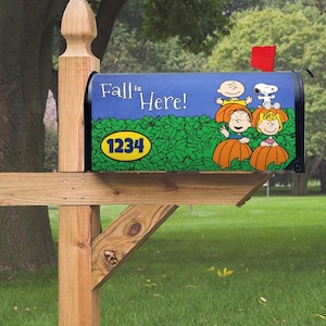 May include: A blue mailbox with a Peanuts theme. The mailbox has a graphic of Snoopy, Charlie Brown, and Lucy holding pumpkins. The text "Fall is Here!" is on the mailbox. The mailbox has a yellow circle with the number "1234" on it.