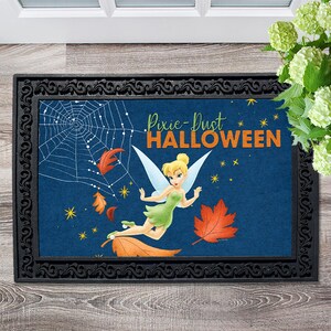 May include: A blue doormat with a black border and a design featuring Tinker Bell flying through the air with a spiderweb and falling leaves. The text "Pixie-Dust HALLOWEEN" is written in orange and yellow letters.