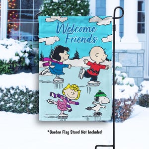 May include: A blue garden flag with the text "Welcome Friends" and a cartoon image of four characters ice skating. The characters are Charlie Brown, Snoopy, Lucy, and Linus from the Peanuts comic strip.