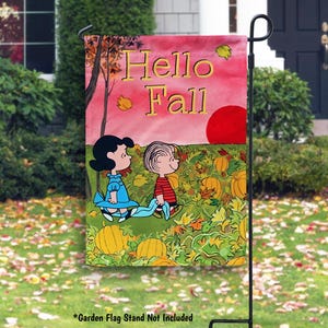 May include: A garden flag featuring a fall scene with the text "Hello Fall." The flag depicts two cartoon children in a pumpkin patch under a pink sky with a red sun. The flag is displayed on a black metal stand.
