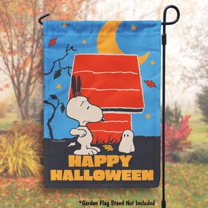 May include: A garden flag featuring Snoopy from Peanuts dressed as a ghost. The flag is blue with a crescent moon and stars. Snoopy is standing in front of his doghouse. The text "Happy Halloween" is printed on the bottom of the flag.