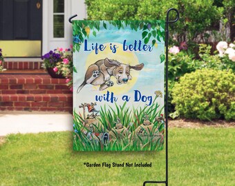May include: A colorful garden flag with a cartoon dog jumping in the air. The flag has a blue sky background with green leaves and the text "Life is better with a Dog".