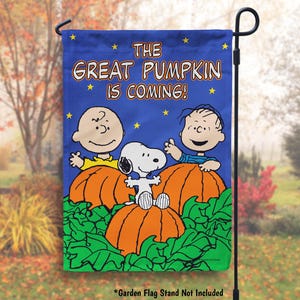 May include: A blue garden flag with the Peanuts characters Linus, Lucy, and Snoopy. The flag says "The Great Pumpkin is Coming!" and features the characters holding pumpkins.