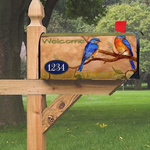 May include: A decorative mailbox with a painted design featuring two bluebirds perched on a branch. The mailbox has the word "Welcome" and the number "1234" on it. The mailbox is mounted on a wooden post with a red flag.