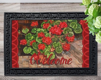 May include: Welcome doormat with a red and green floral design featuring geraniums in pots. The doormat has a black border with a decorative pattern.