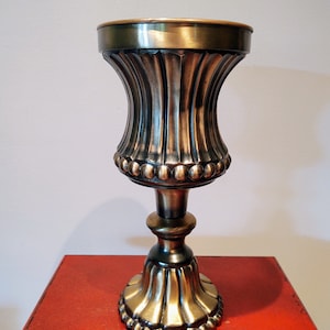 Op de afbeelding: Een gouden metalen vaas met een geribbeld ontwerp en een parelrand. De vaas heeft een hoge, slanke voet en een brede, ronde opening.