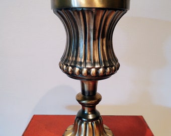 May include: A gold-toned metal vase with a fluted design and a beaded rim. The vase has a tall, slender base and a wide, round opening.