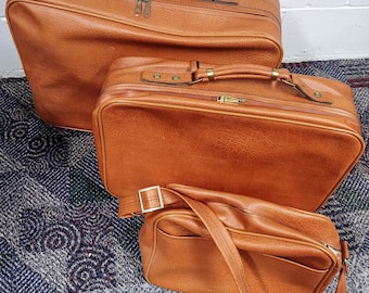 Puede incluir: Conjunto de tres maletas de cuero marrón con un aspecto vintage. La maleta más grande tiene un asa superior y las dos maletas más pequeñas tienen asas superiores y correas para el hombro.