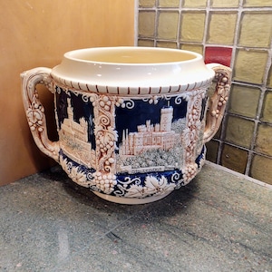 May include: A white ceramic pitcher with blue and brown details. The pitcher features a castle scene and the text "Stolzenfels Rhein".